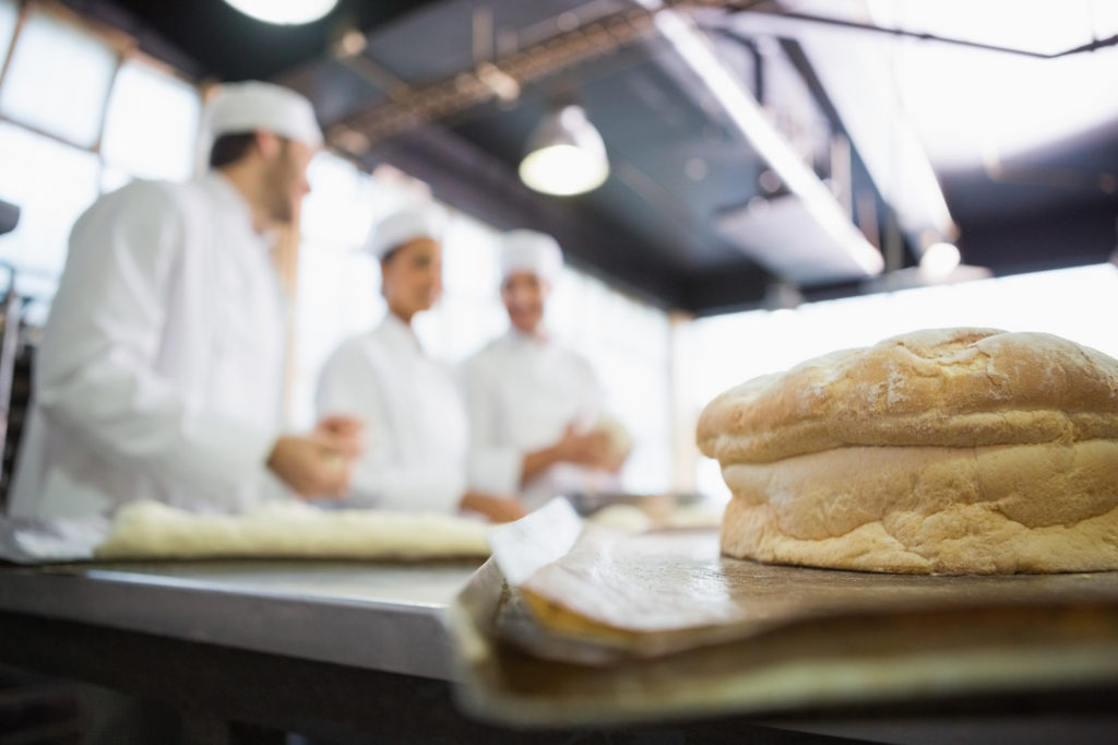 Fresh bread with bakers behind him in the kitchen of the bakery